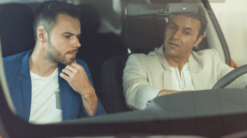 A car owner and a car buyer sitting in the front seats of a second-hand car, looking over its features.