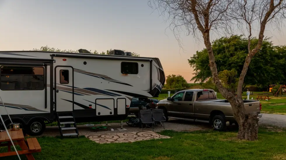 A person holding a roadworthy certificate in front of a parked camper trailer.