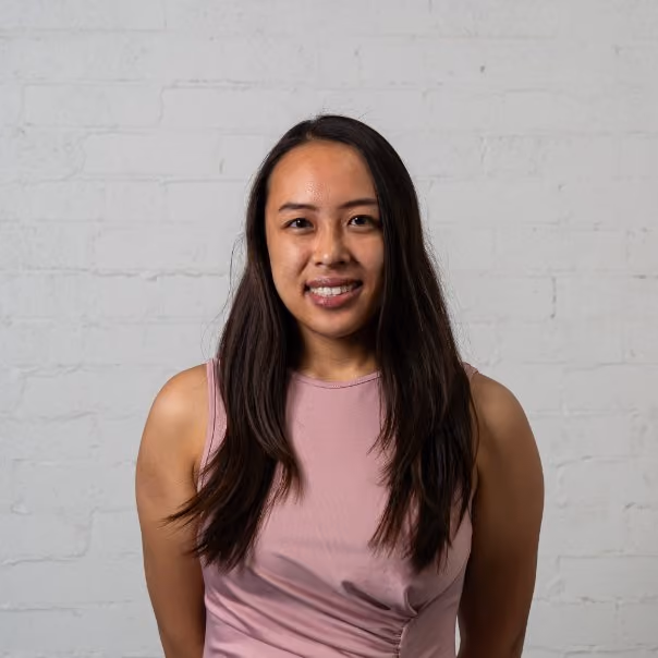 Smiling woman in pink top standing against white brick wall