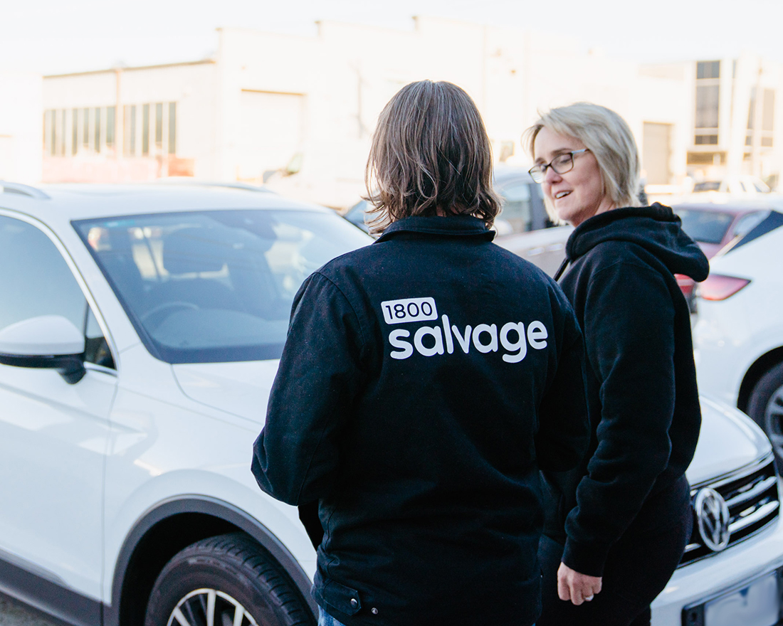 1800 Salvage team member speaking with a customer beside a white Volkswagen SUV.