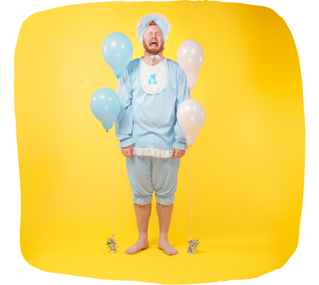 Person dressed in a blue baby costume, standing barefoot between blue and white balloons with a crying expression against a bright yellow background.