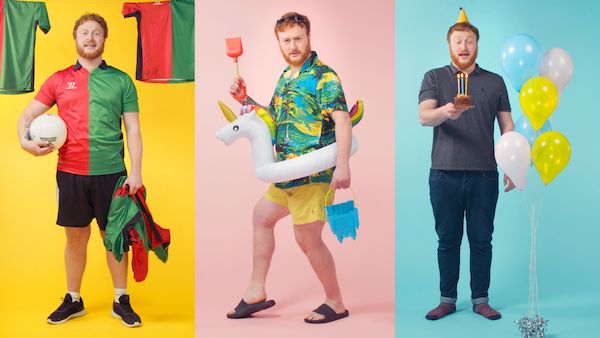 Three men, one in a football kit, another in a Hawaiian shirt with a t.unicorn swim ring on and lastly a man standing by balloons blowing out candles on a cake.