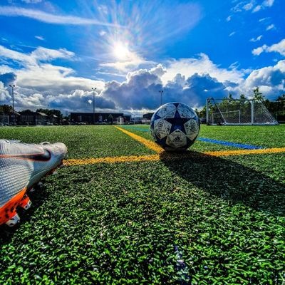 A football and football boot on a pitch in the sun 