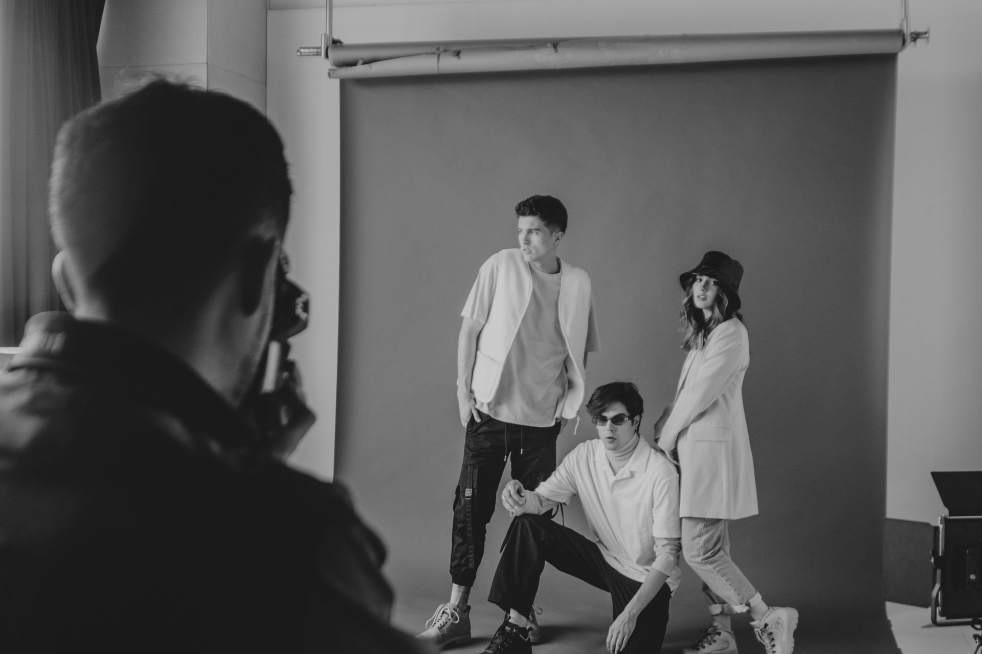 Black and white picture of a photoshoot showing a photographer taking a picture of 3 people in a studio.