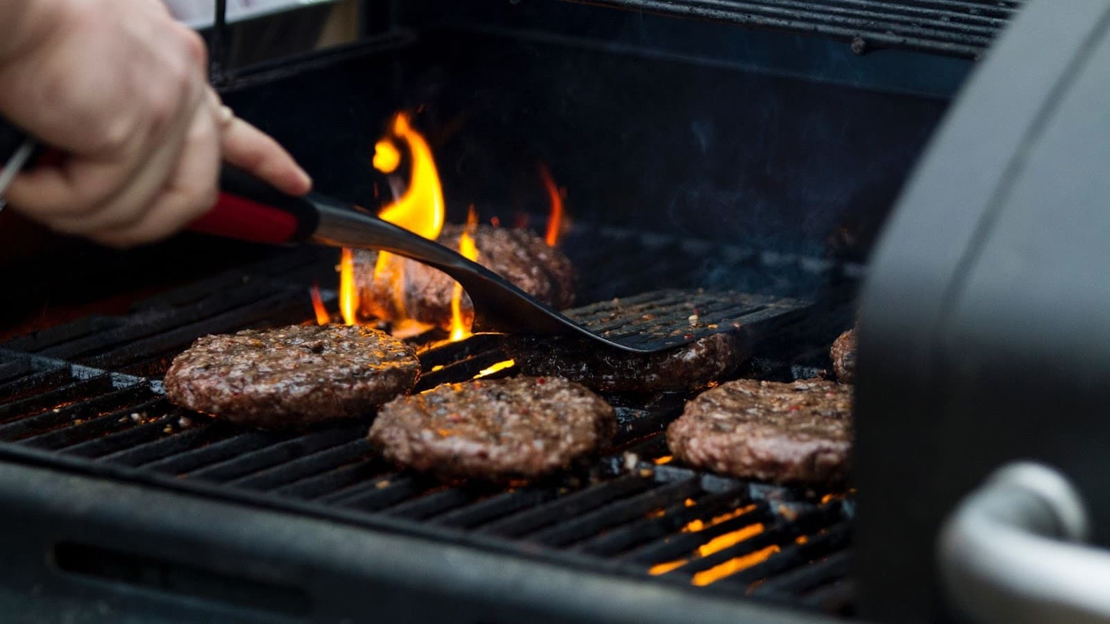 A person tending to a barbecue with burgers on it 