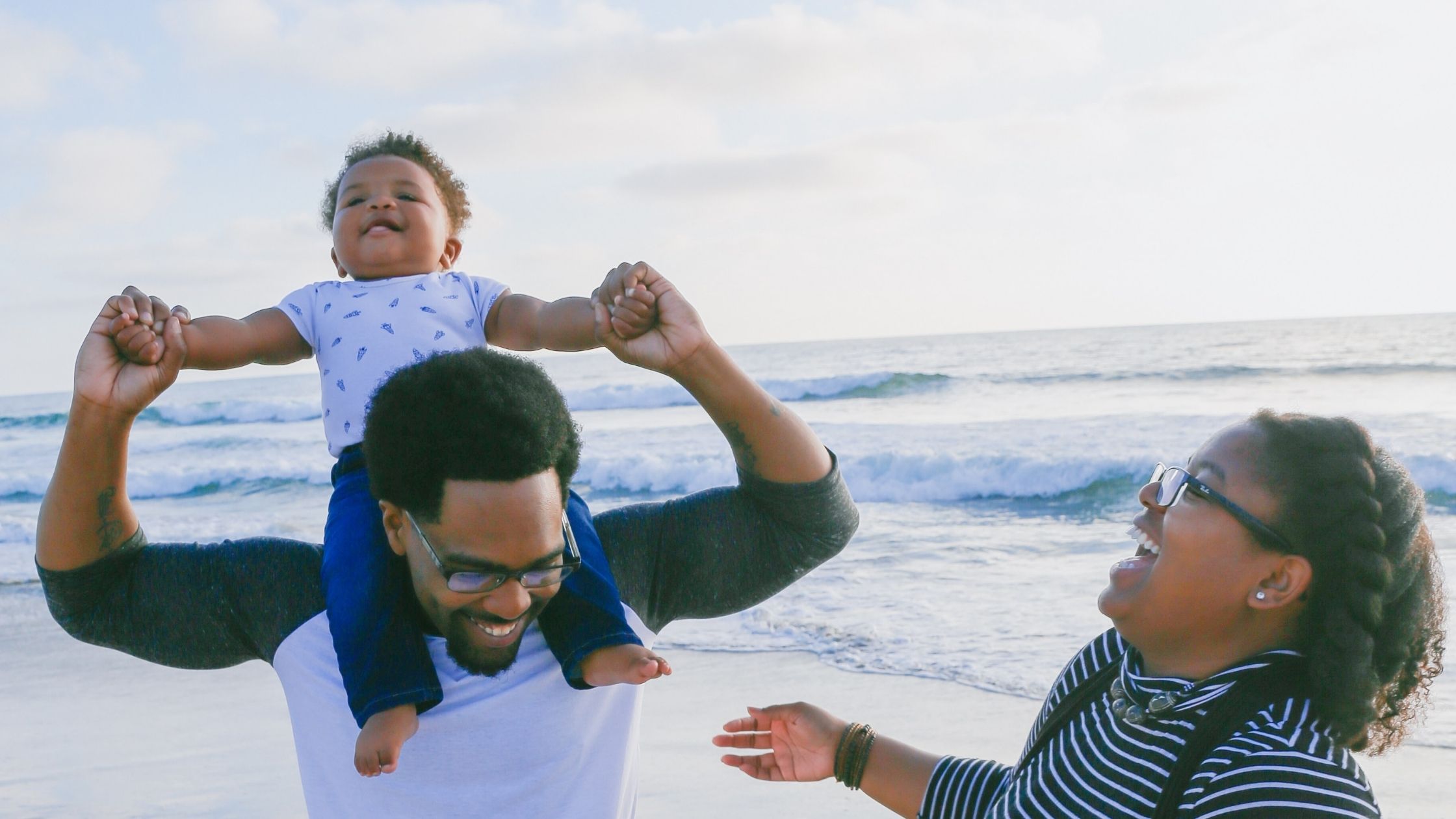 A family on the beach with the baby on her fathers shoulders