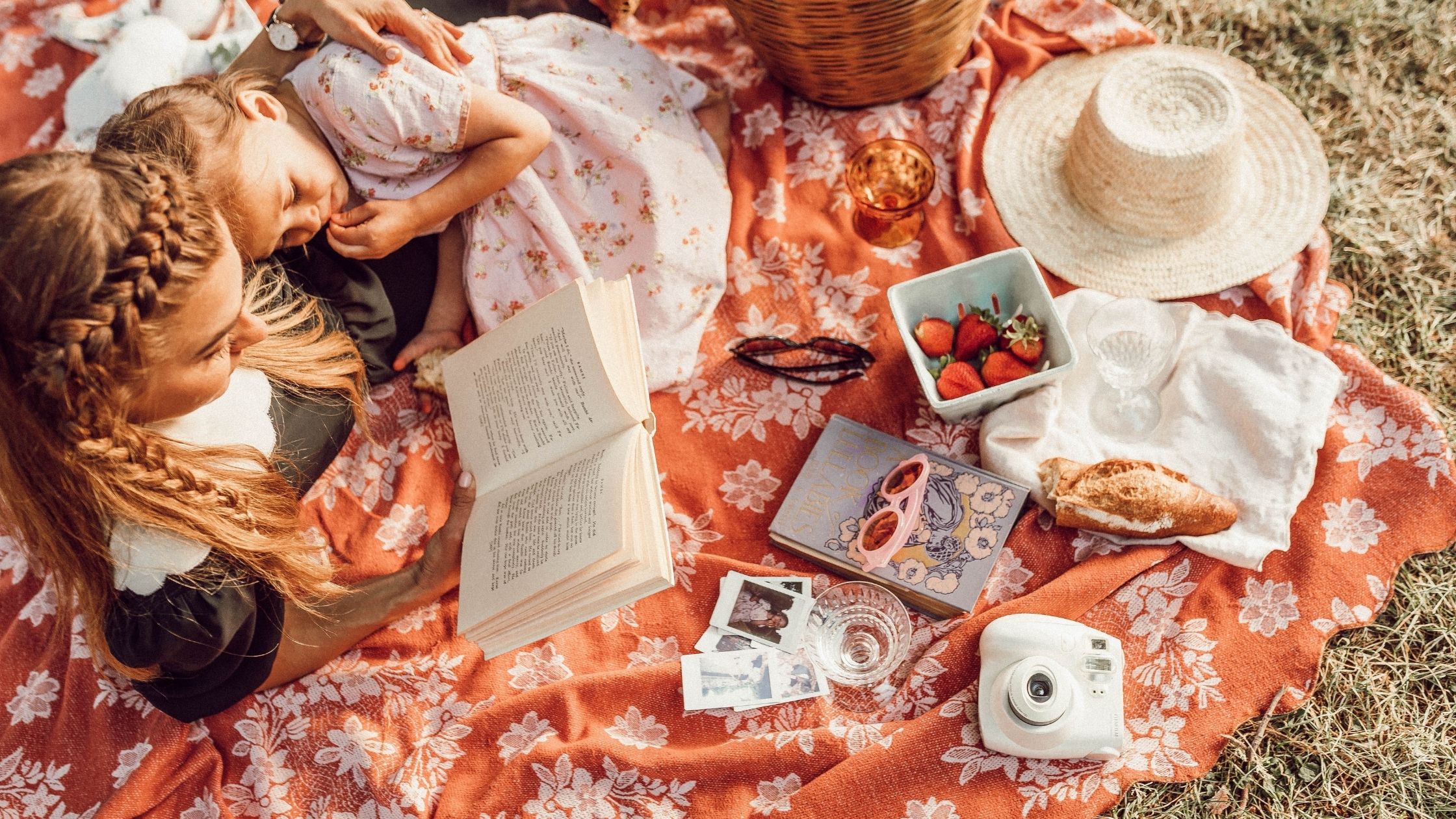 A Mother and daughter read a book on a picnic blanket