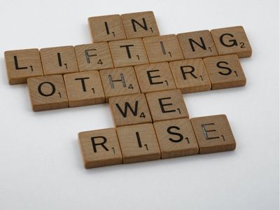 Scrabble tiles saying 'In lifting others we rise' 