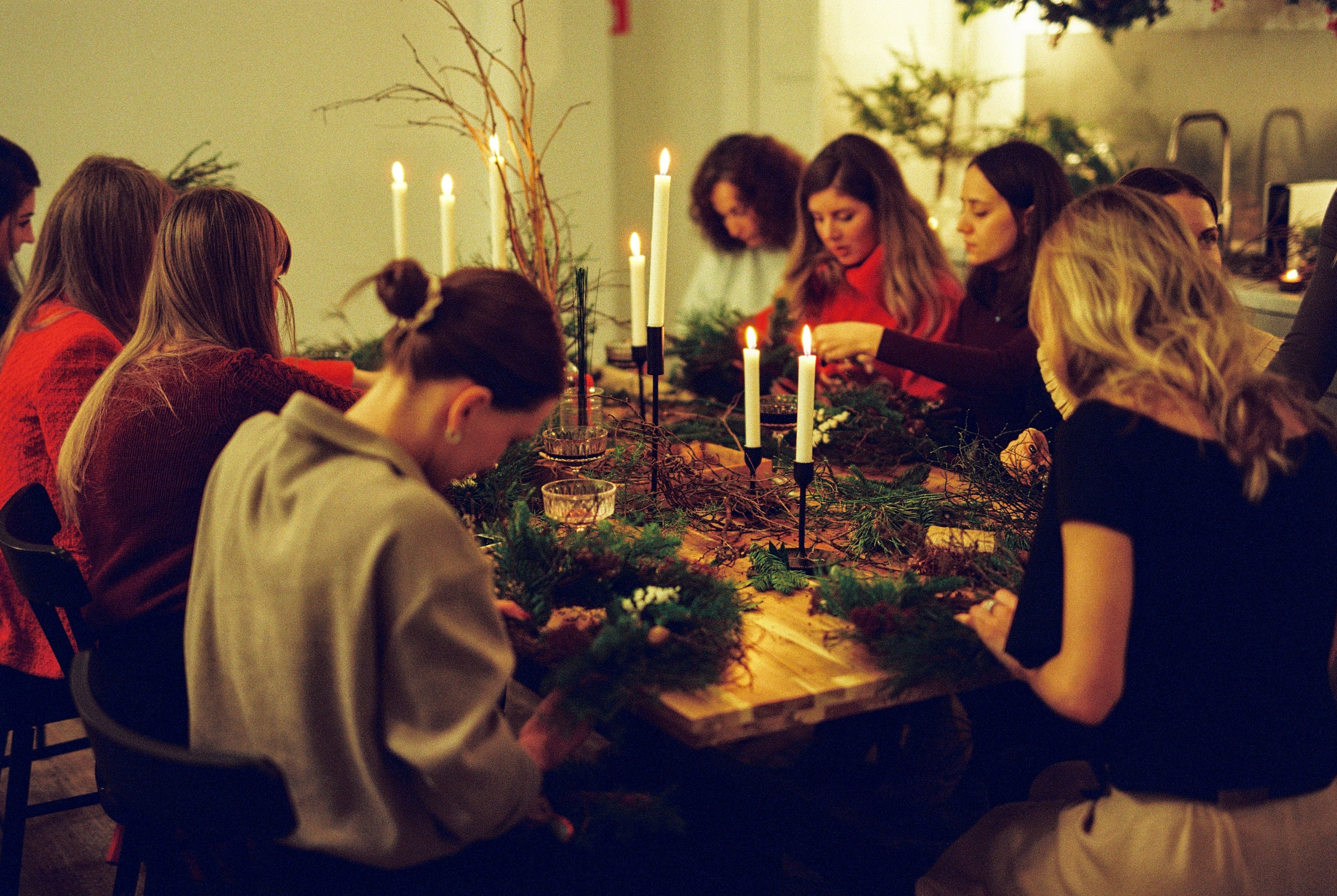 A wreath making workshop with women sat around a able making wreath in candlelight room.