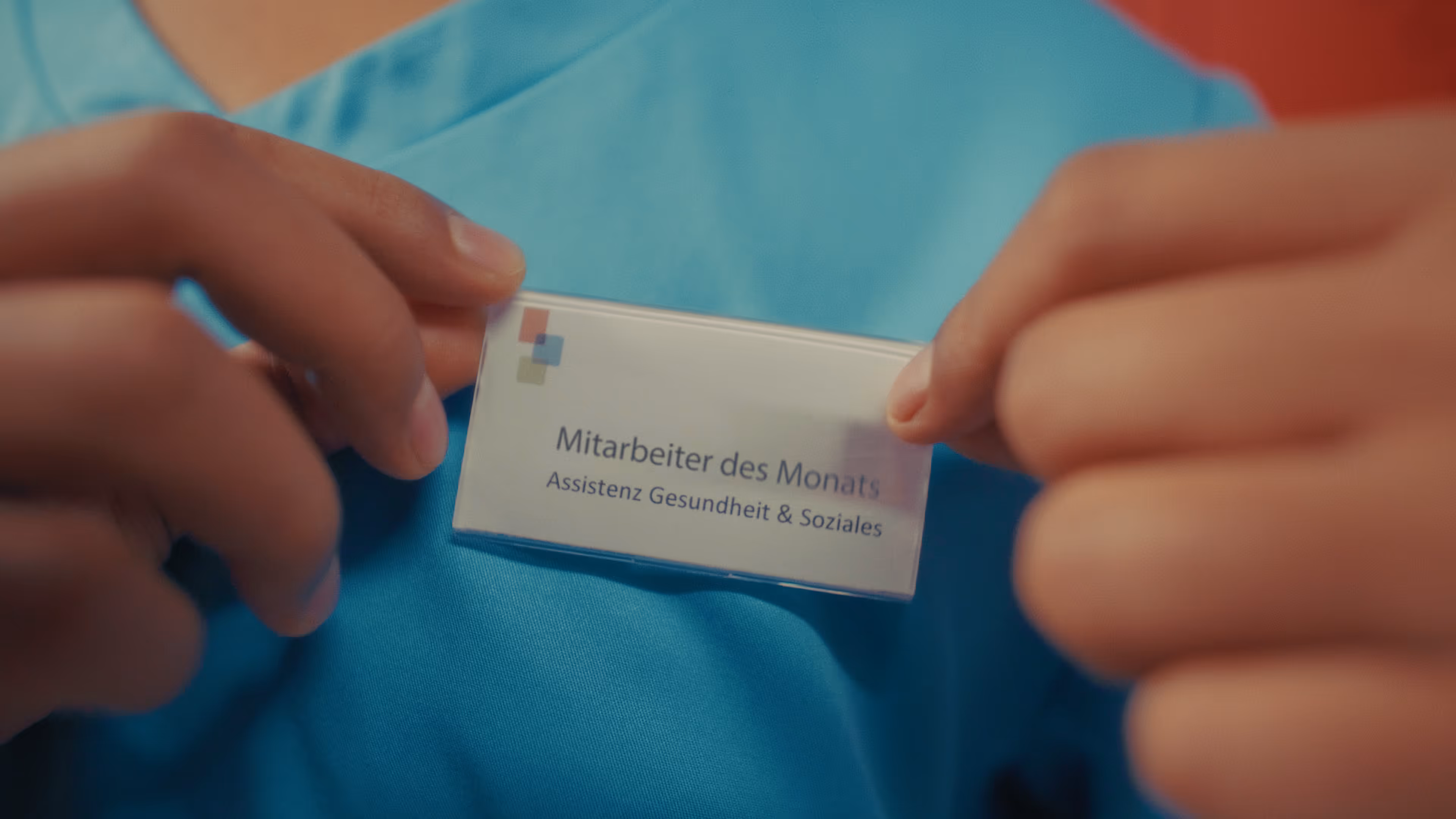 Nahaufnahme einer Person in blauer Kleidung, die eine Karte hält mit der Aufschrift Mitarbeiter des Monats.