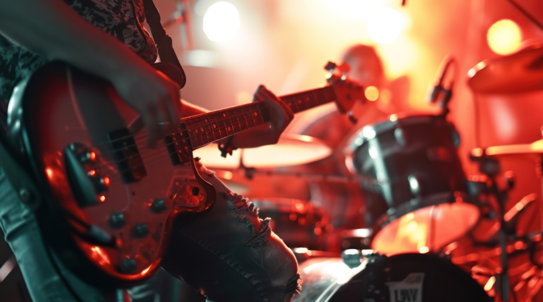 Musiker spielt E-Bassgitarre, während im Hintergrund ein Schlagzeuger unter warmer Bühnenbeleuchtung auftritt.