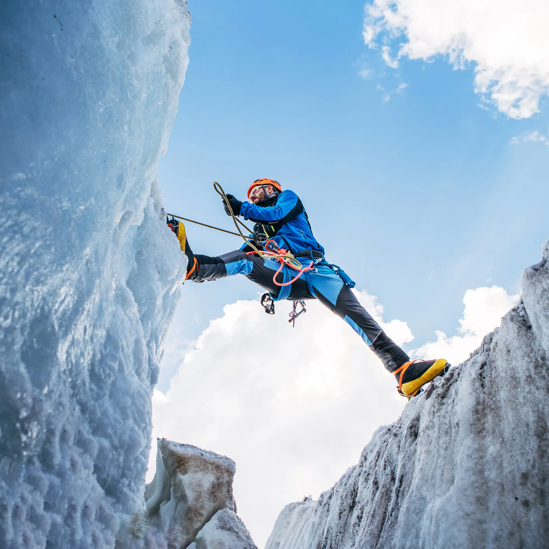 Mountain climber scaling an icy cliff against a bright blue sky.