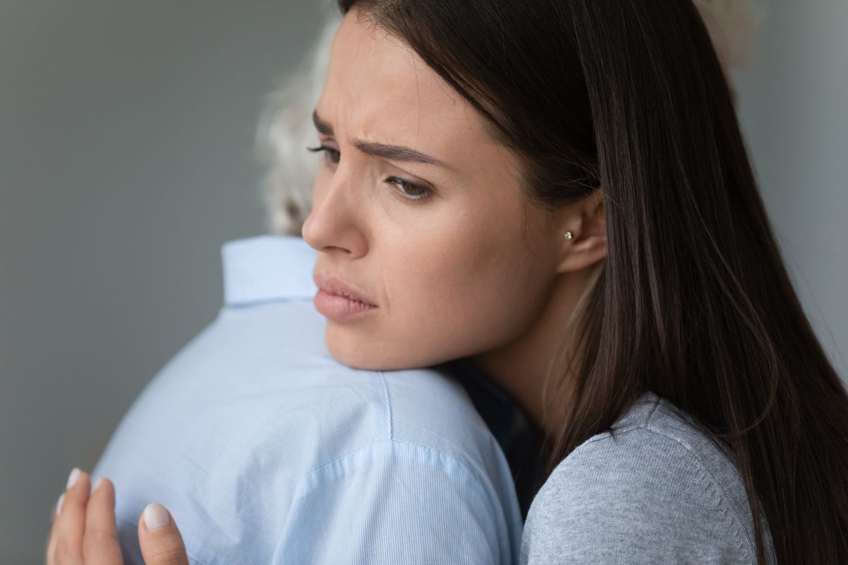 A young woman with a pained expression hugs an older person closely, conveying comfort, sorrow, and emotional support.