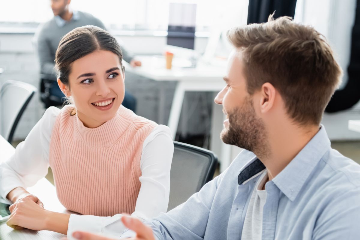 Smiling businesspeople talking near computers and notebook on table in office