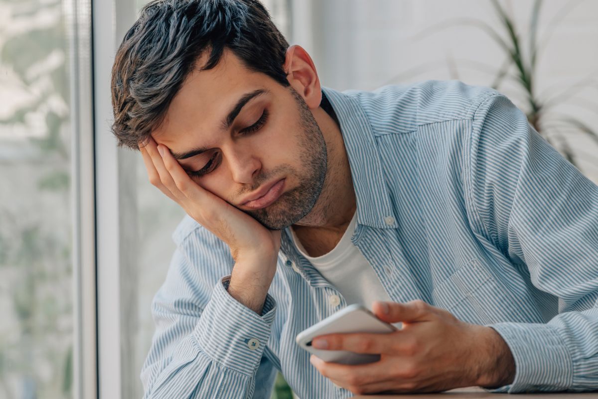 young man at home bored looking at mobile phone