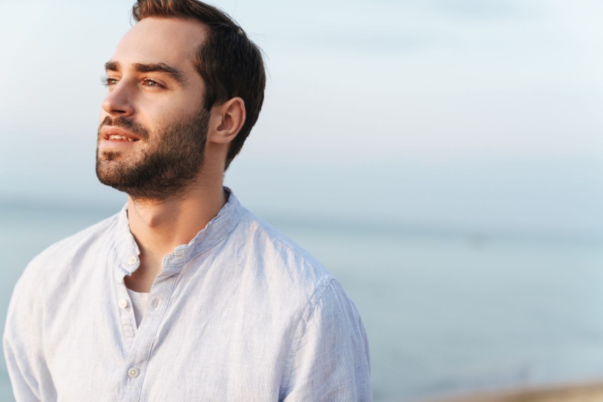 Close up of a handsome young bearded man looking off into the distance at a beach