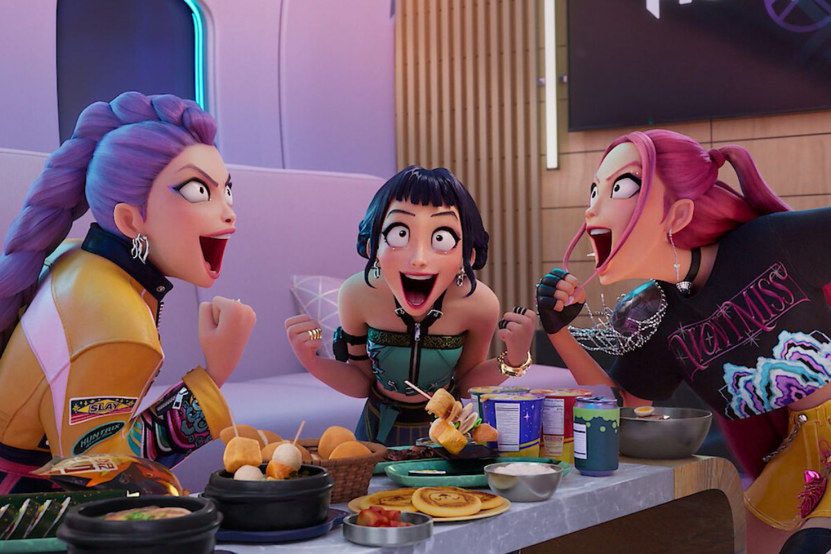 he animated HUNTR/X trio from KPop Demon Hunters cheer excitedly around a table full of food in a playful, high-energy moment; all images courtesy of Netflix.