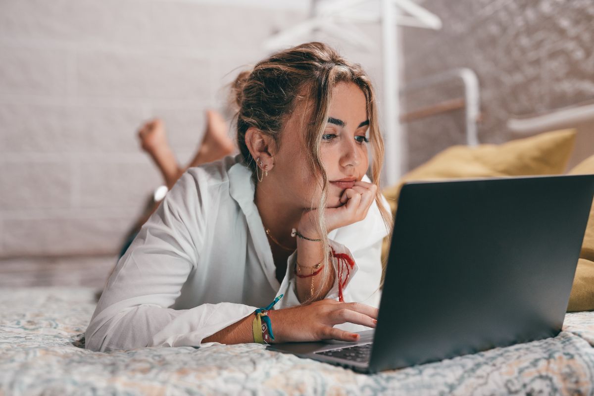 Close up of one young pretty woman using laptop indoor at home lying on the bed surfing the net.