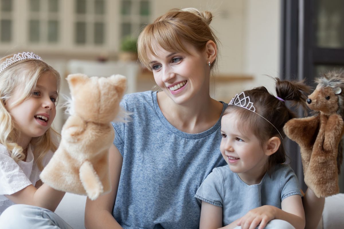 Adult woman and two young girls happily play with forest animal puppets.