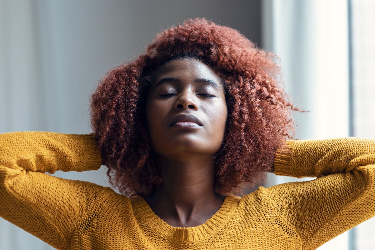 Young black woman with red hair holding hands behind head and breathing deeply