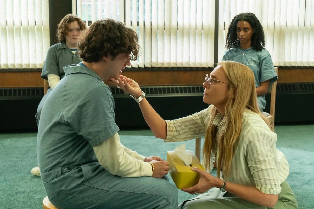 A group therapy scene from Netflix’s Wayward shows a distressed teen being gently comforted by an adult woman holding a tissue box, while other teens watch quietly in the background.