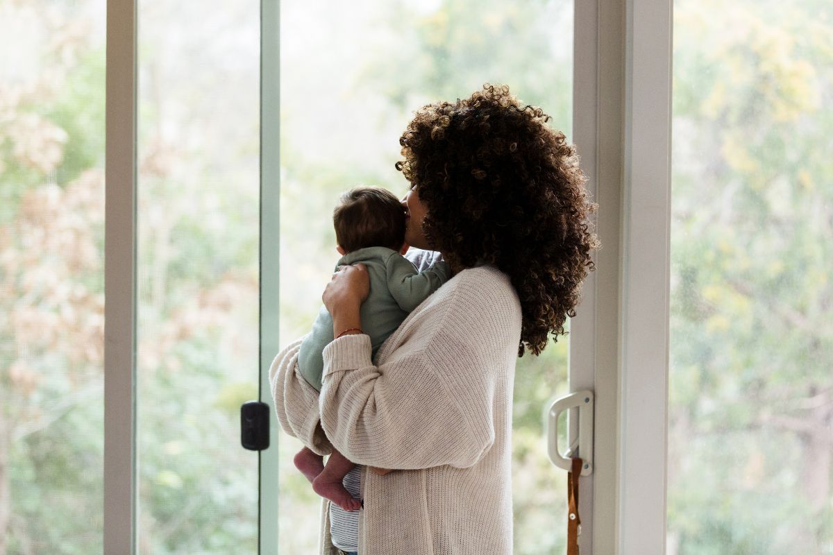 Mom happily holding baby close while stand in front of sliding doors that open up to nature