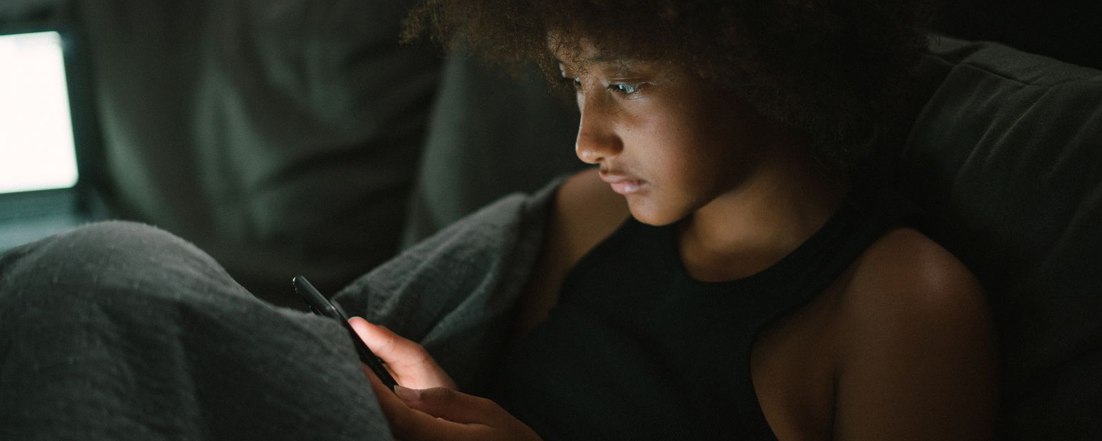 Black woman scrolling on her phone in bed in a dark room 