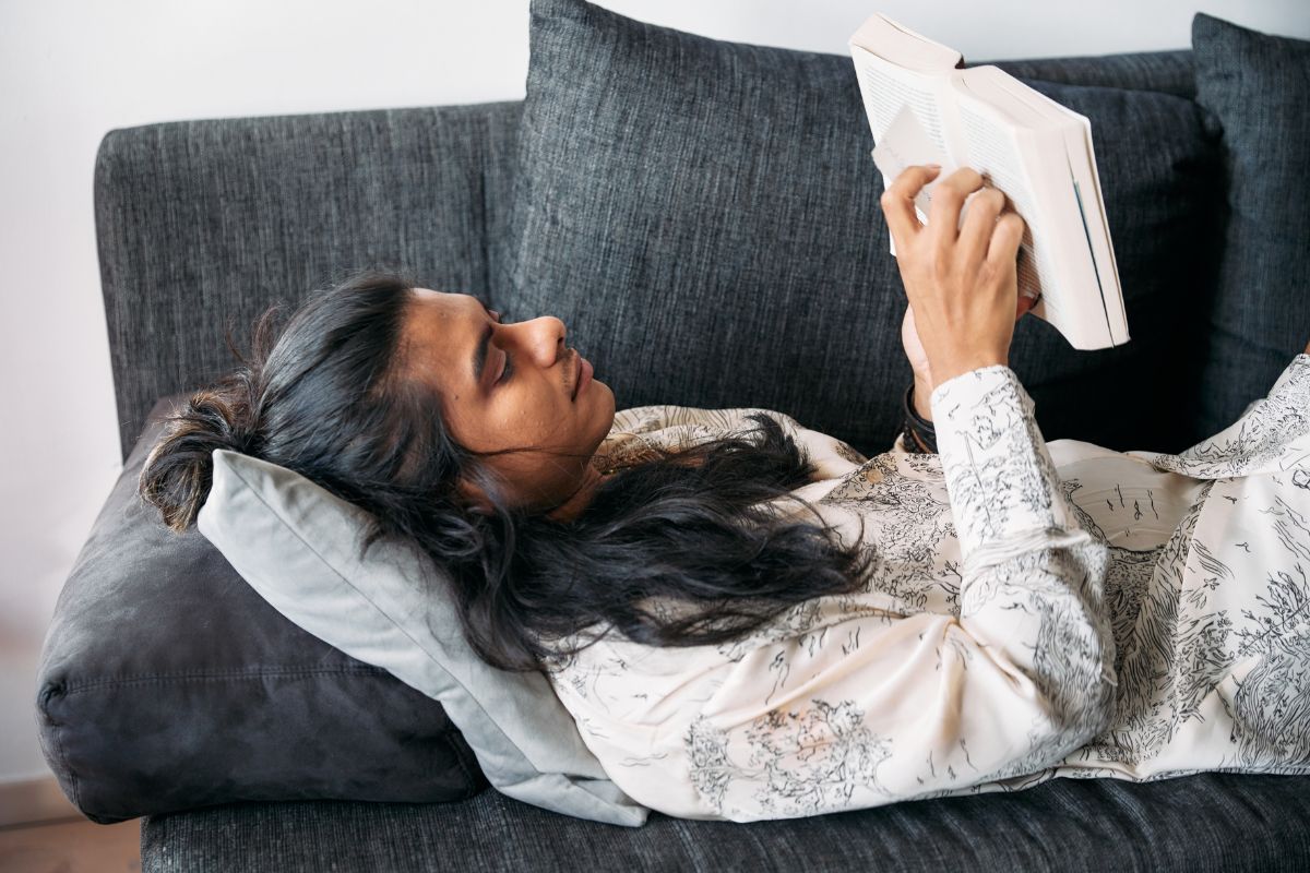 Gender fluid person laying a couch happily reading a book