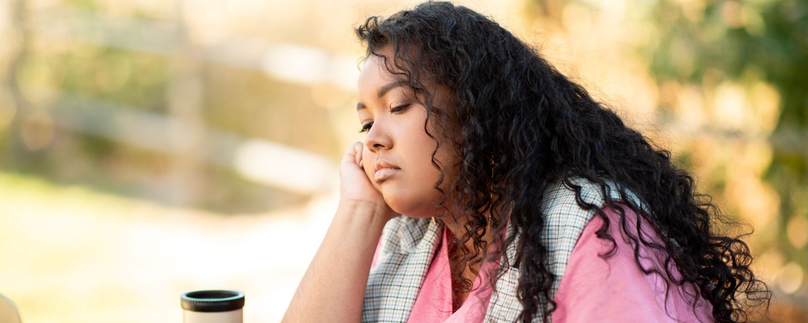 Tired and burnout AAPI woman sitting at the park with an empty cup looking low. 