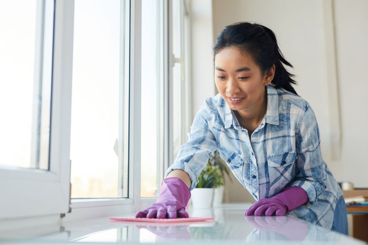 Portrait of young Asian woman washing windows and smiling happily while enjoying Spring cleaning