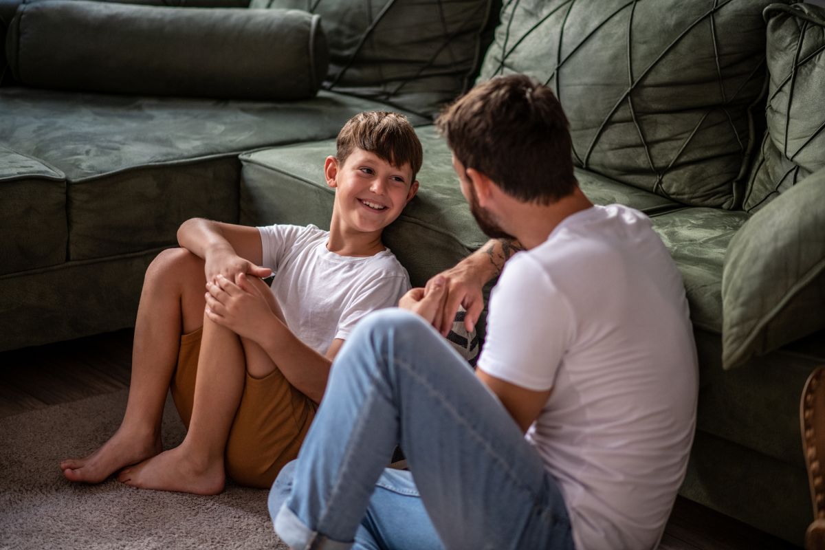 Father and son sit on the living room floor and talking and smiling