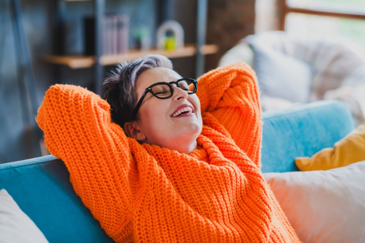 Cheerful middle aged woman sit comfy sofa closed eyes hands behind head free time chill apartment indoors