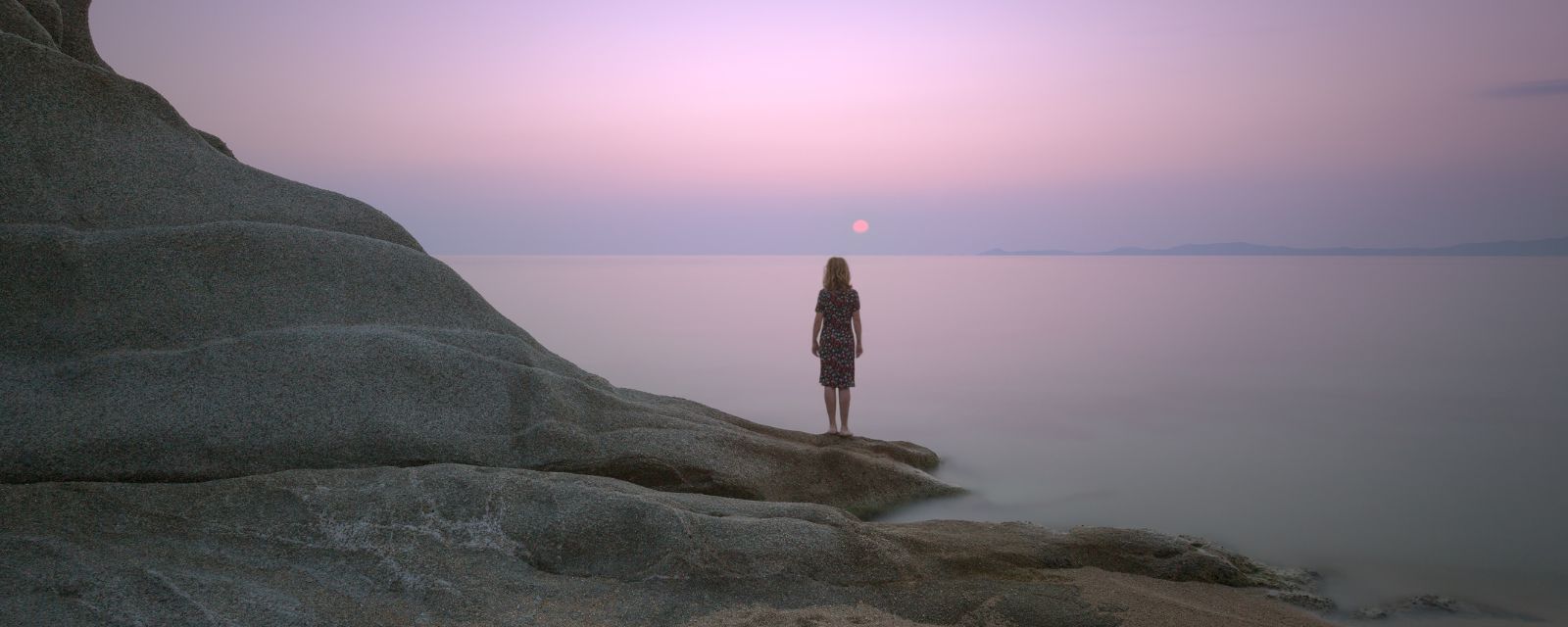 Tranquil seascape scene with woman looking at the sunset 