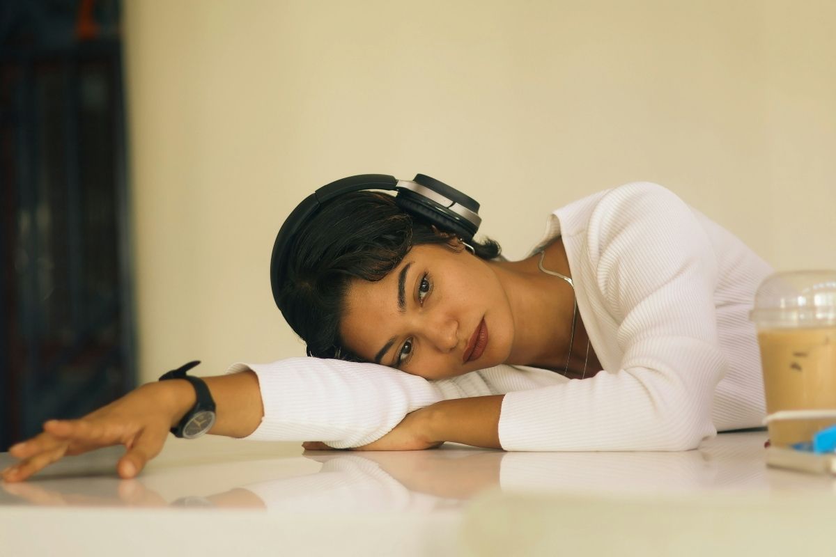 Young woman listening to music with headphones laying head and arm on table looking melancholic.