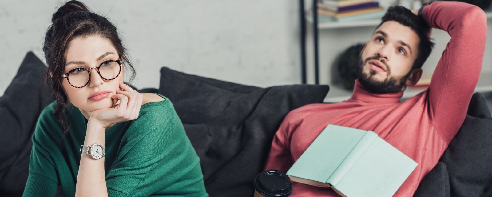 Bored White woman in glasses and sitting near handsome White man with paper cup and a book resting on his chest as he is looking up at the ceiling bored as well
