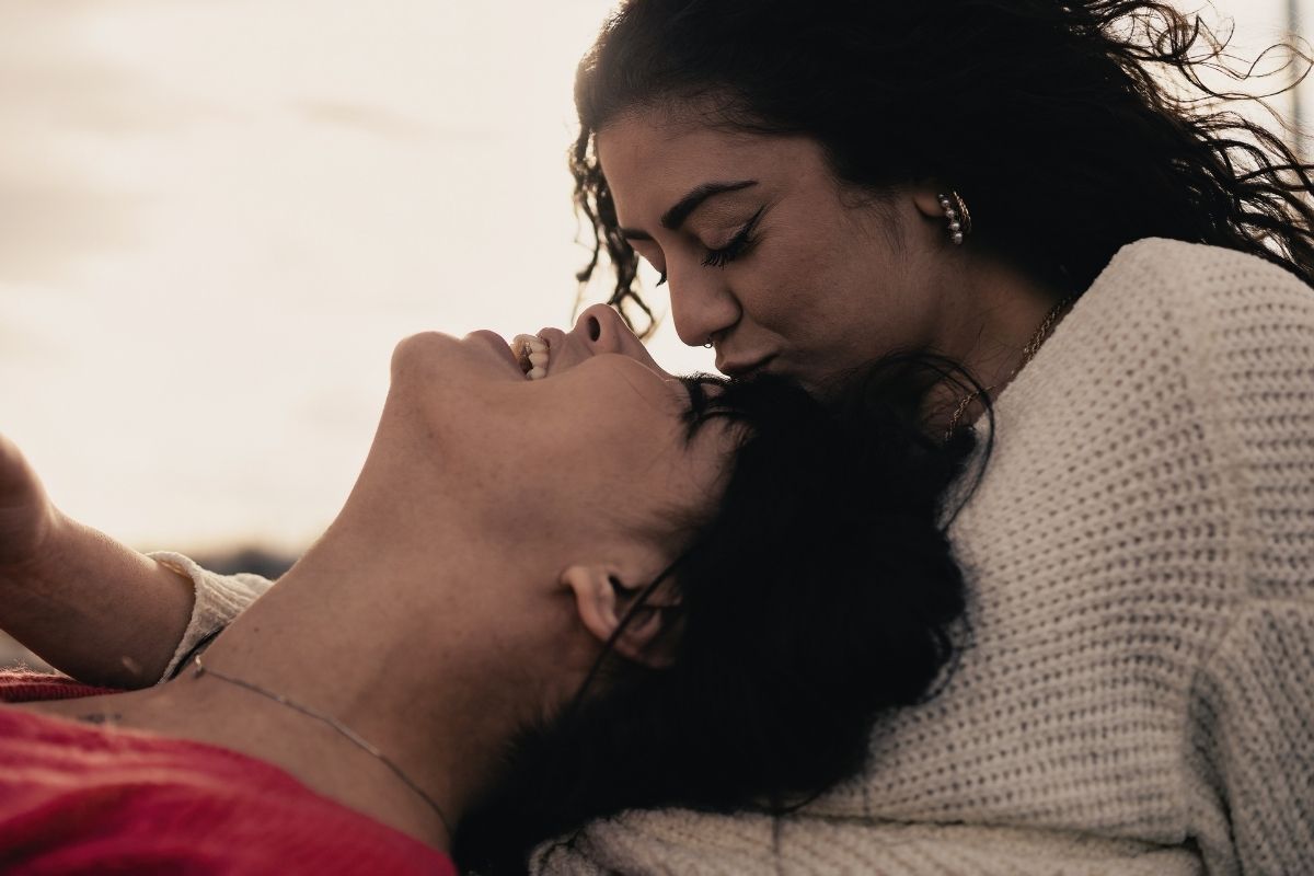 Tender and authentic moment of a young lesbian couple at sunset. Intimate connection and love shown with a gentle kiss on the forehead.