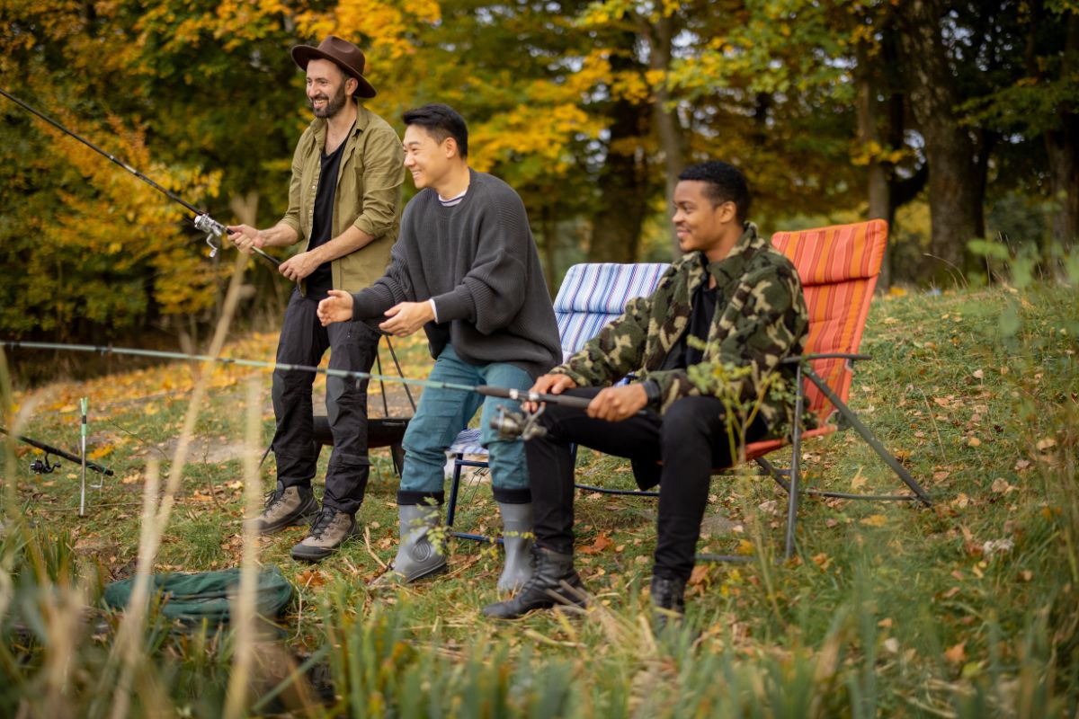 Pleased multiracial male friends resting and fishing on river.