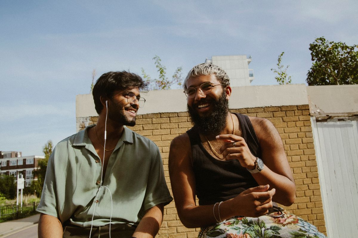 Two young multiracial men hanging out in street style clothes and having fun listening to music with earphones