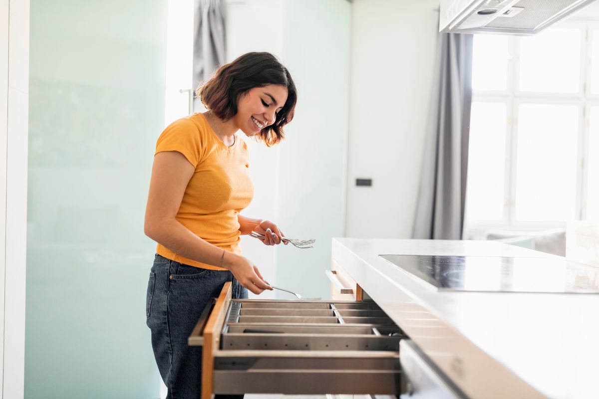 Smiling Middle Eastern female tidying up cutlery in kitchen drawer