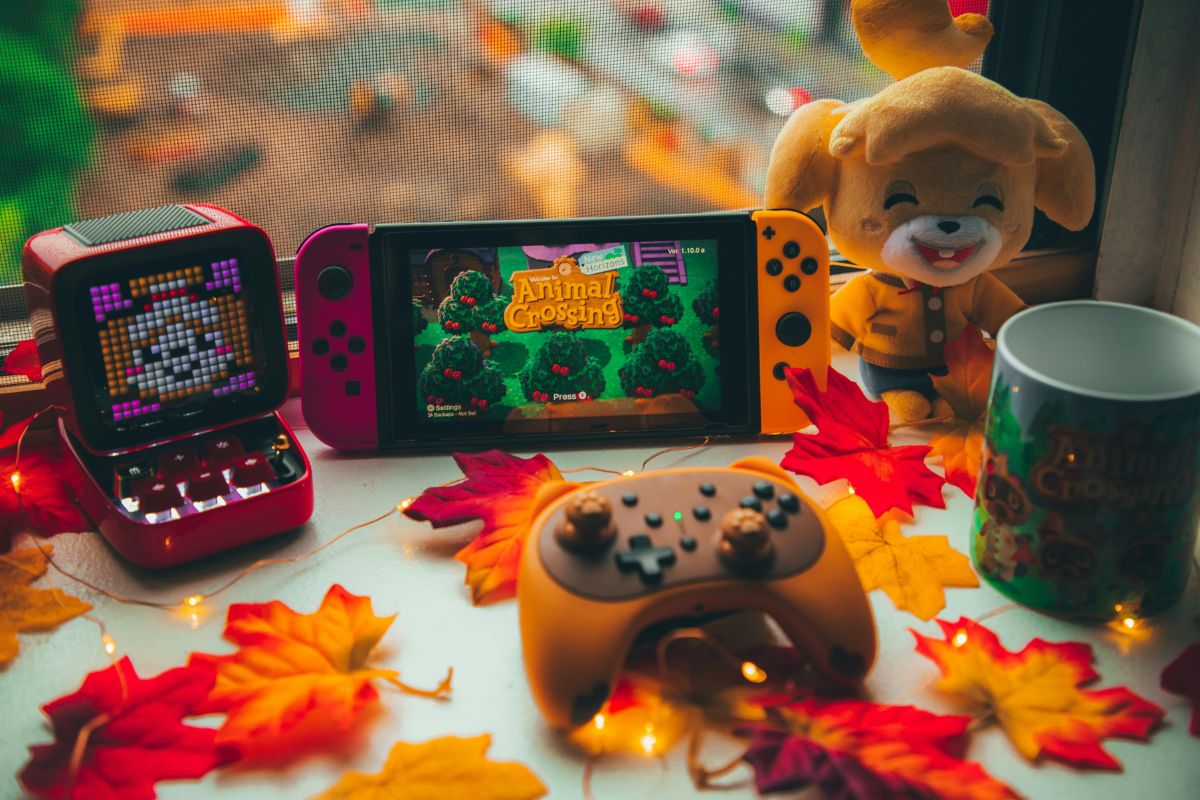 Aesthetic image of video game set up with switch showing Animal Crossing start screen, an orange controller in front, and other animal crossing merch including a stuffed animal and mug.