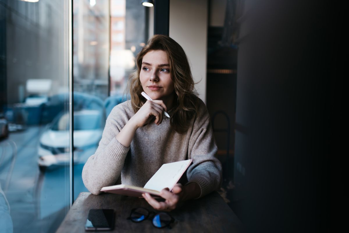 Pensive White woman thinking with notebook at table