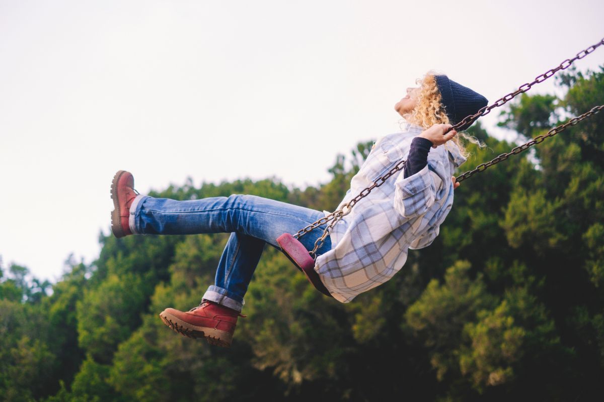 Joyful and youthful woman flying high on a swing at the childhood park.