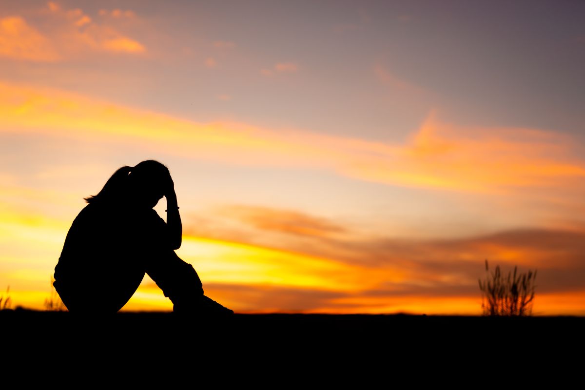 Silhouette of sad and depressed women sitting at walkway of park with sunset