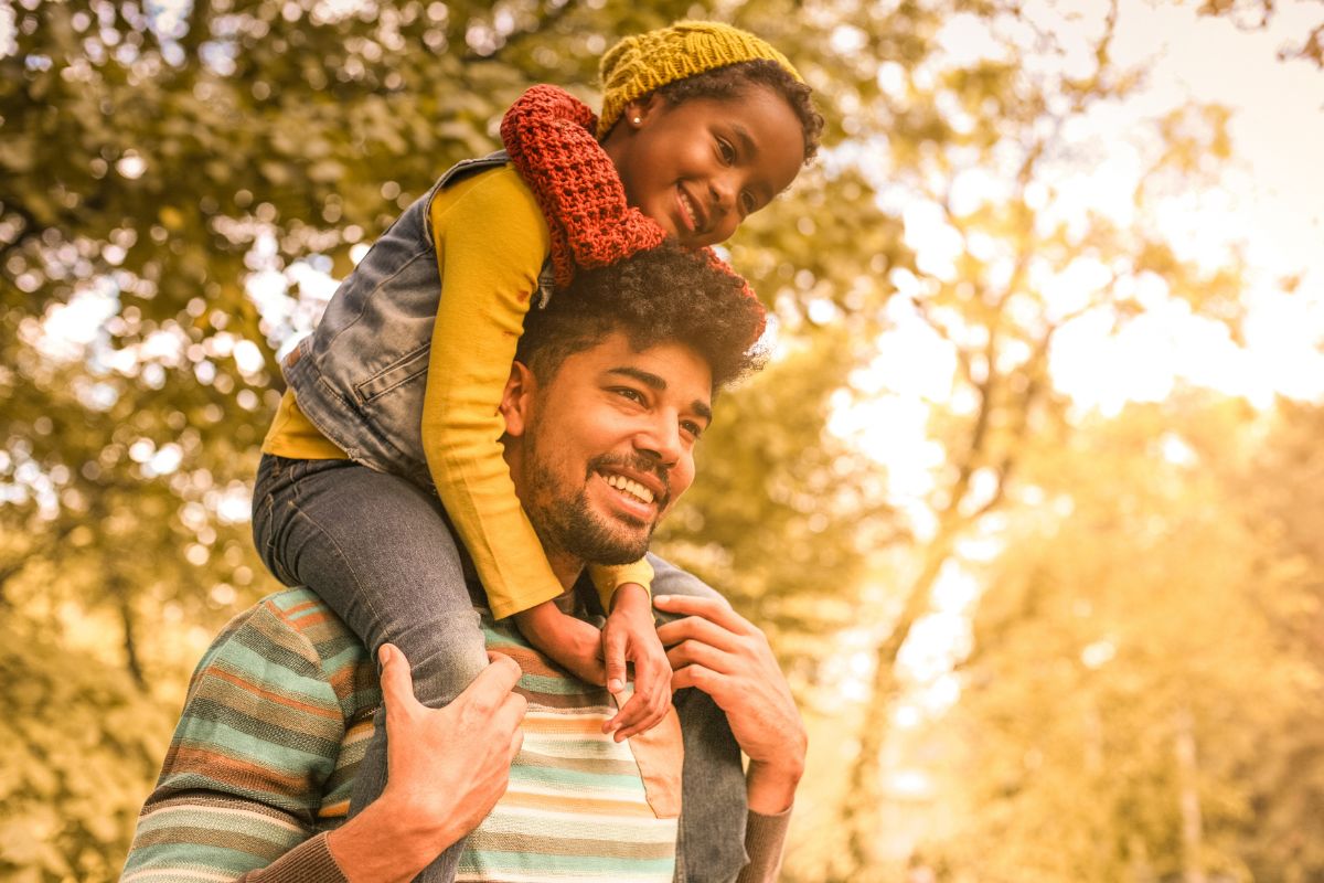 African American father holding sun on shoulders on an autumn afternoon.