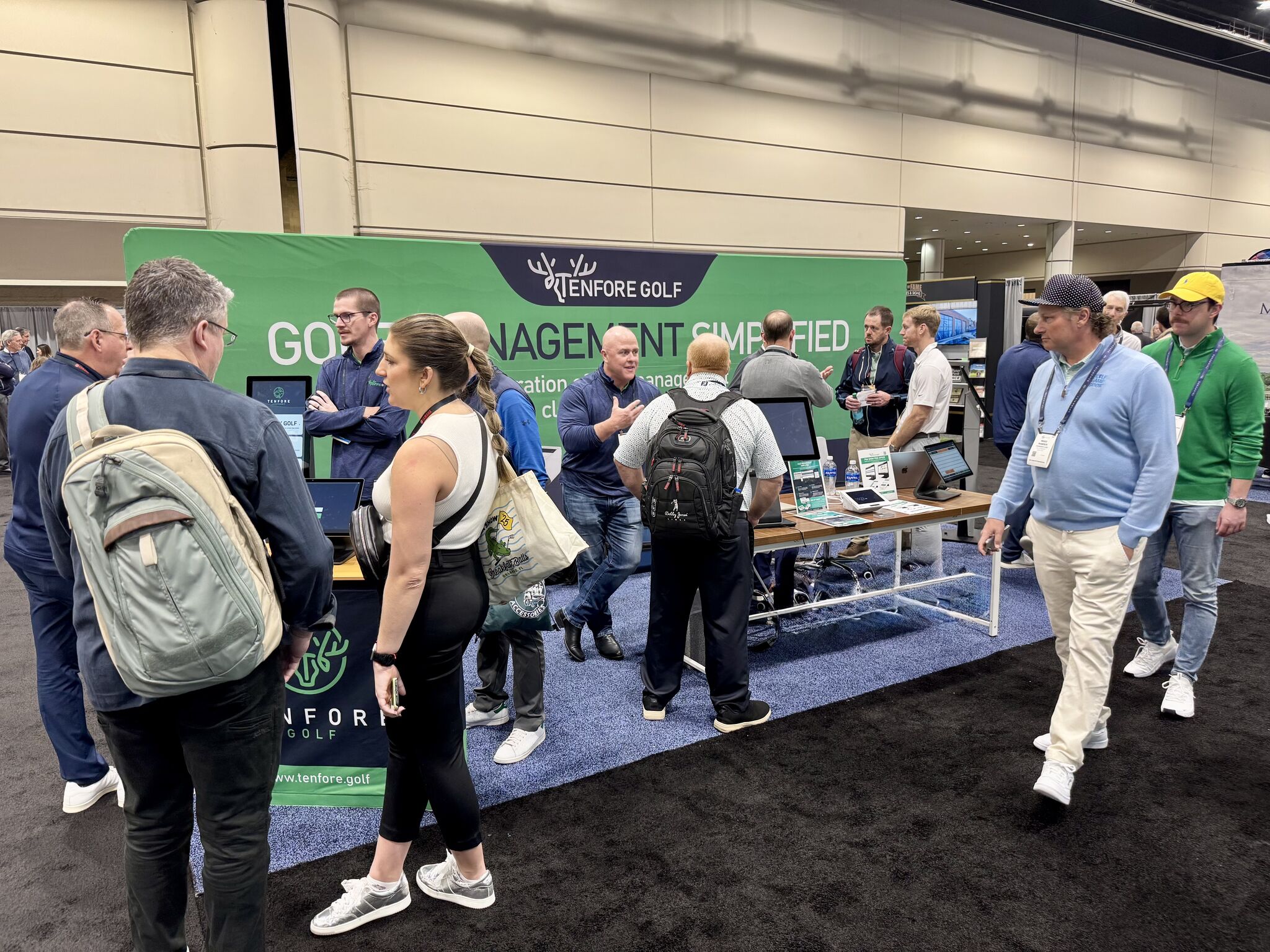 TenFore Golf staff talking with visitors at their trade show booth, beside a self-service check-in kiosk and point-of-sale terminals