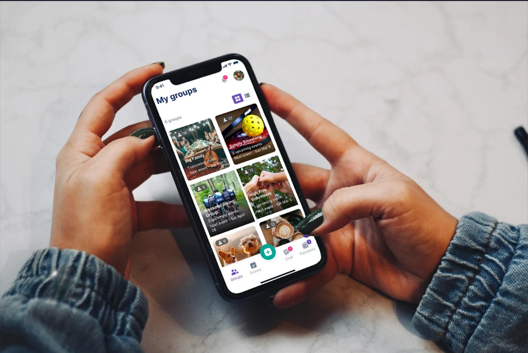 Hands holding a phone showing the HeyConnect My groups screen, with group events and chat and payments tabs