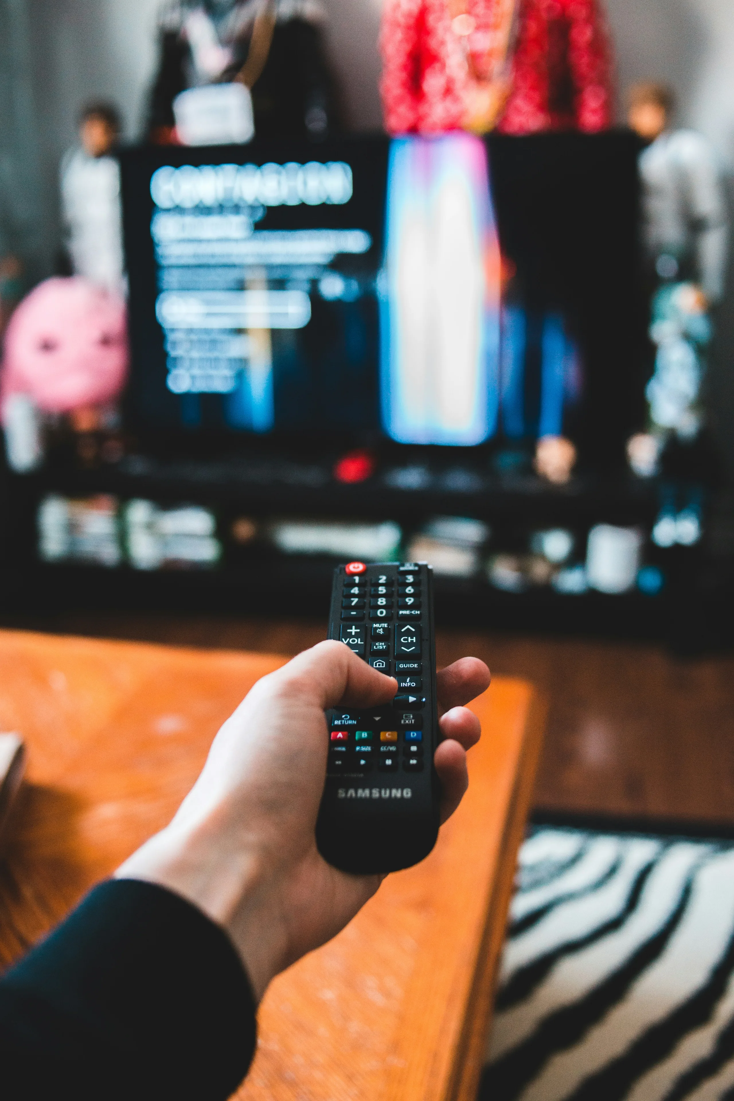 A hand holding a TV remote controller pointed at a screen