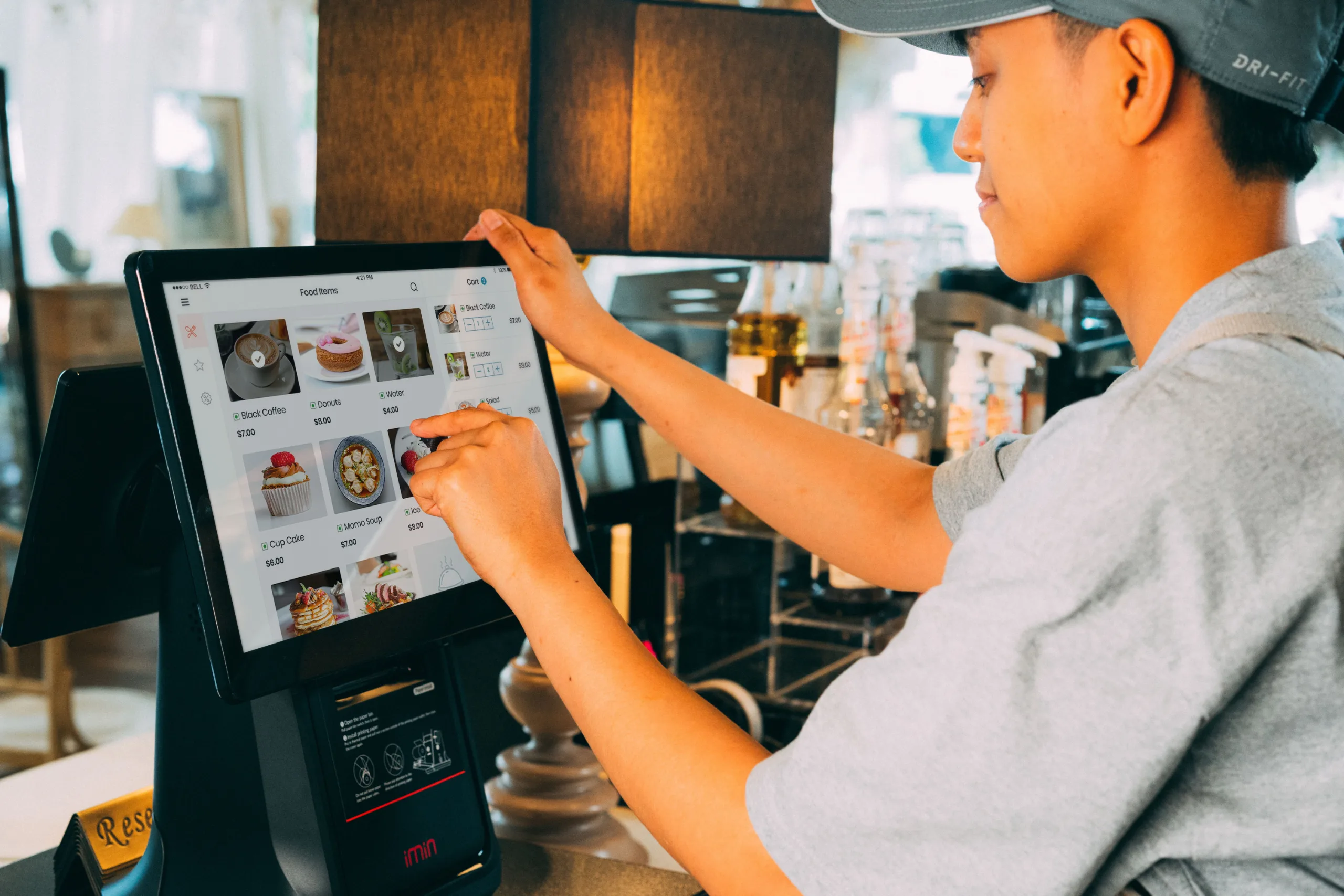 A cafe worker taking an order on a countertop point-of-sale screen during a shift