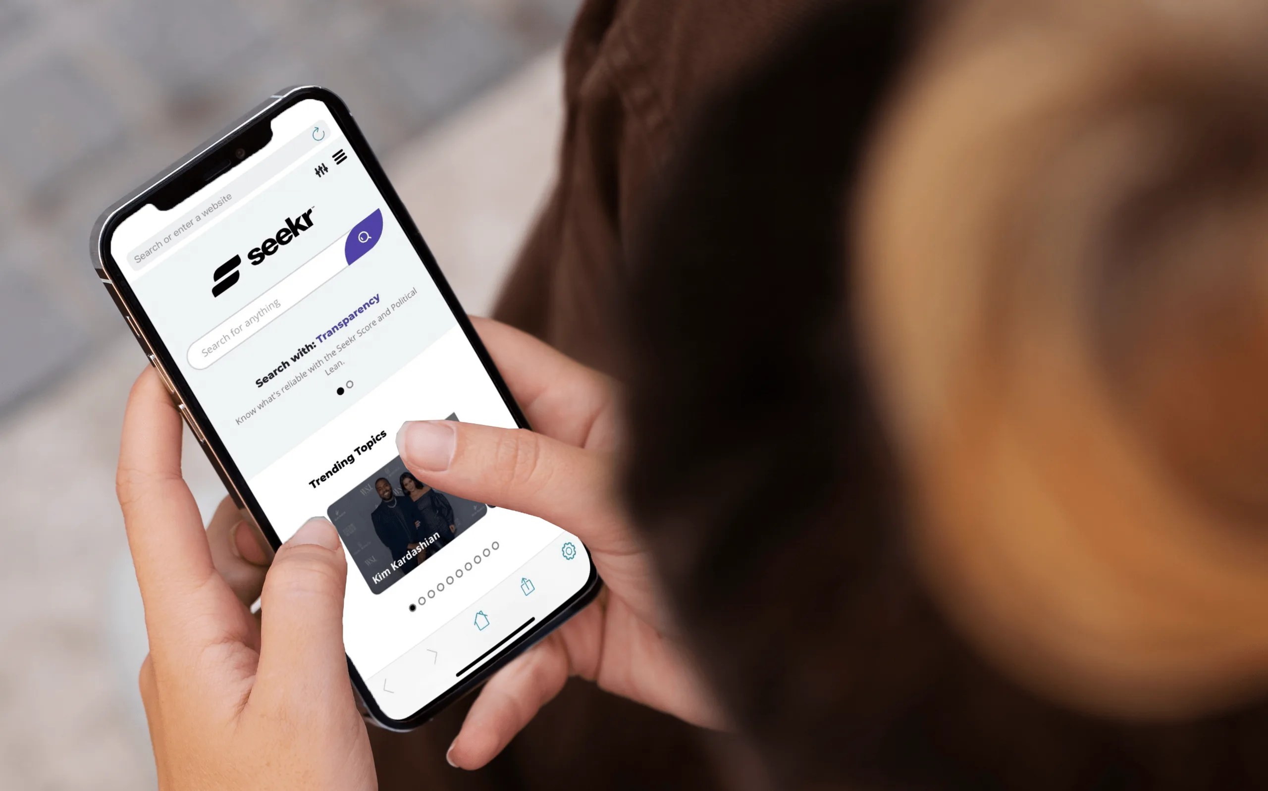 Someone using the Seekr app on a phone, showing its search bar and the prompt Know what is reliable with the Seekr Score