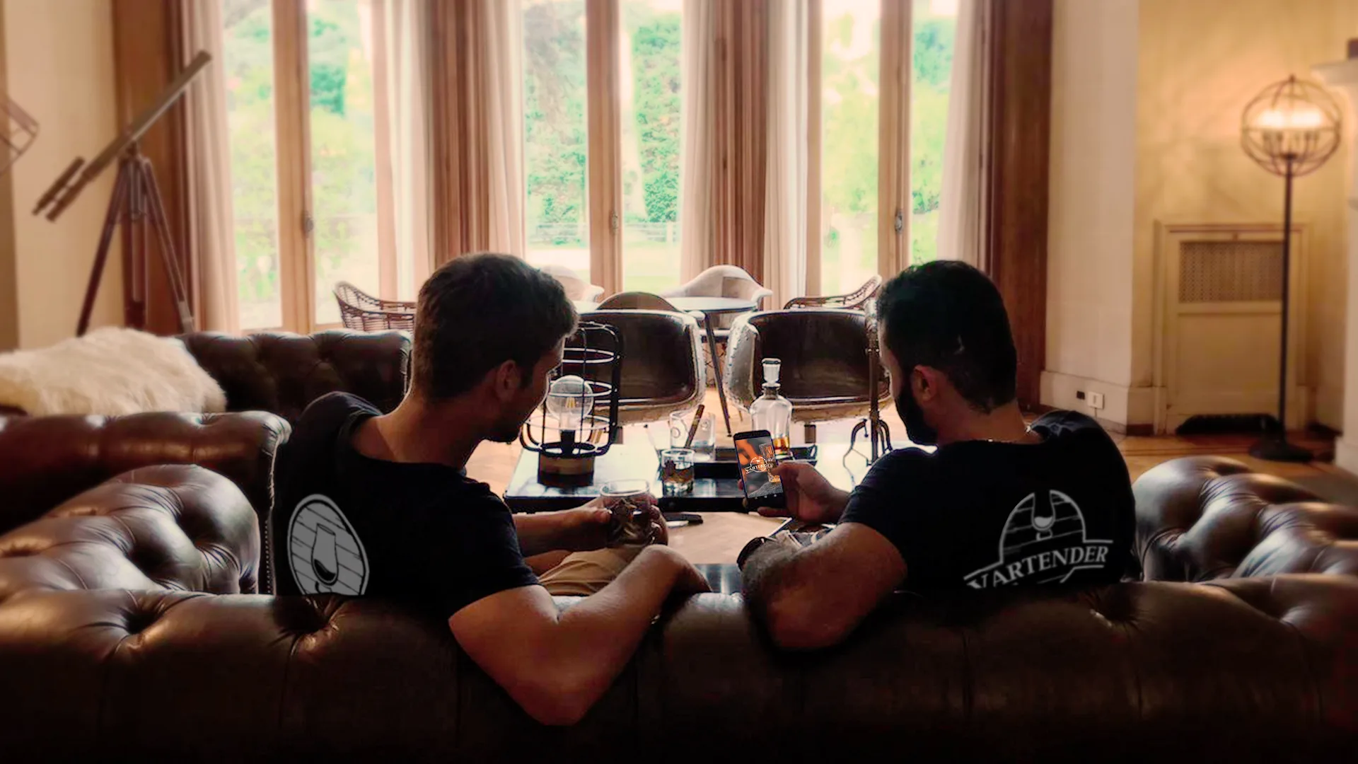 Two people wearing Vartender's tshirts sitting on a couch drinking whisky and using the app